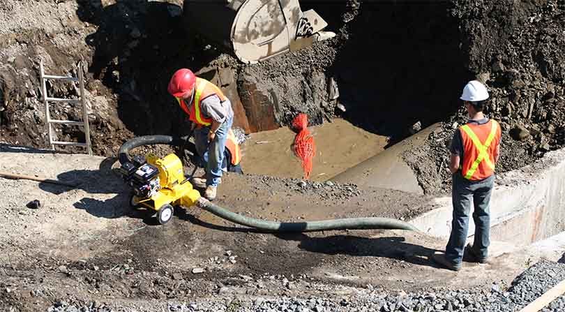 Construction workers using a pump to remove water from a job site