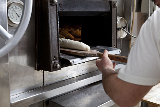 
Baker removing fresh bread from a commercial oven in a food and beverage production setting